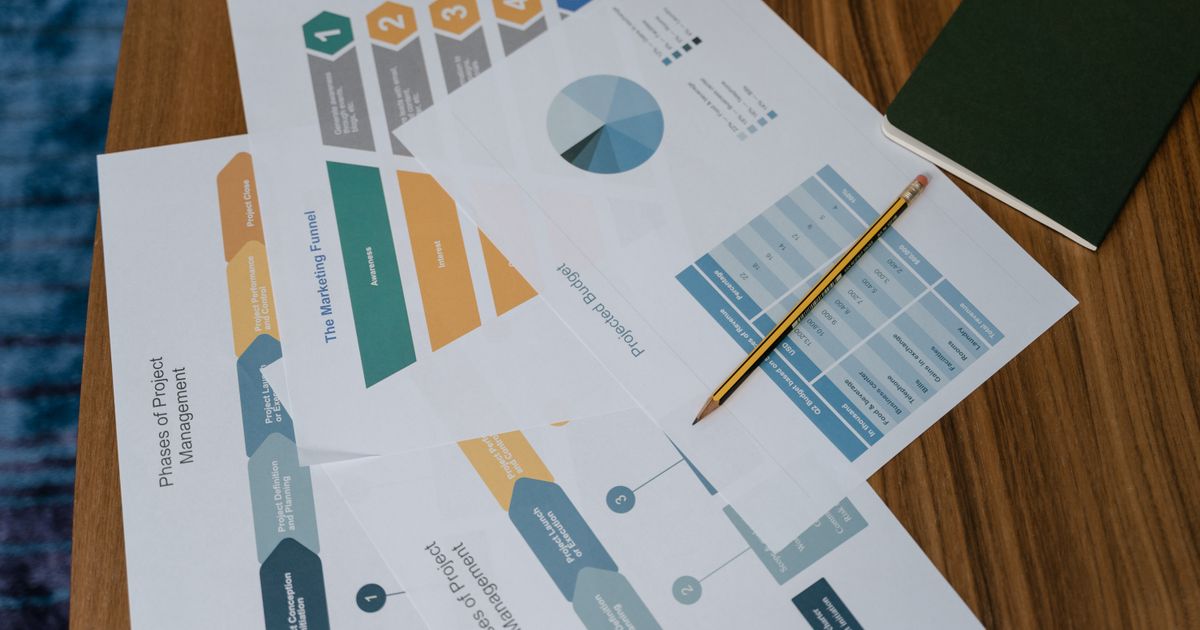 Overhead view of project management documents and charts on a desk with a pencil.