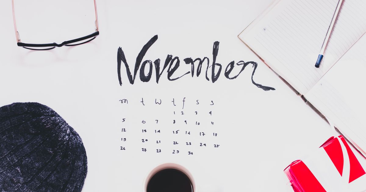Flat lay of a November calendar with cozy autumn accessories, warm sweater, and hot coffee.