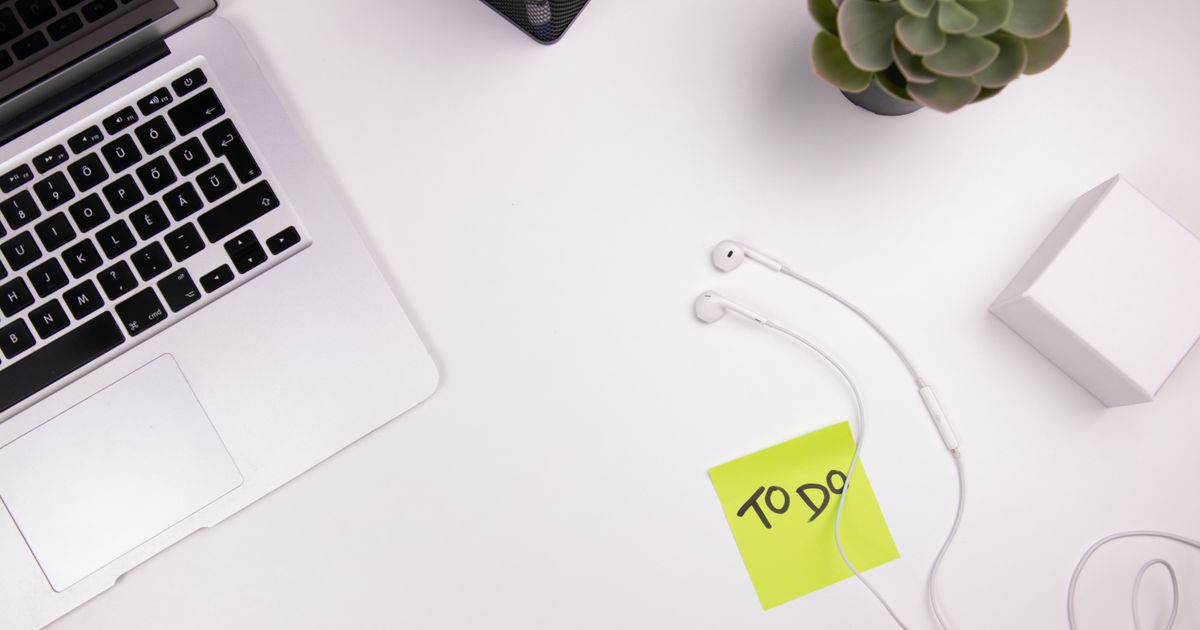 Organized workspace featuring a laptop, earphones, and a to-do list with plant decor.