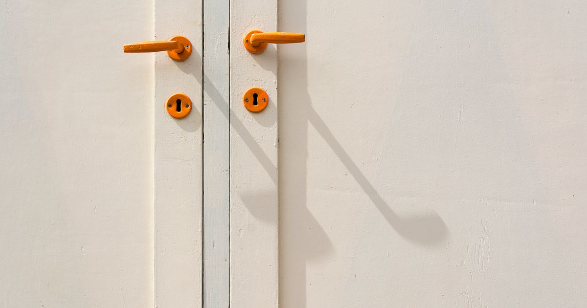 Minimalist close-up of a white door featuring orange handles and shadows, creating modern aesthetic.