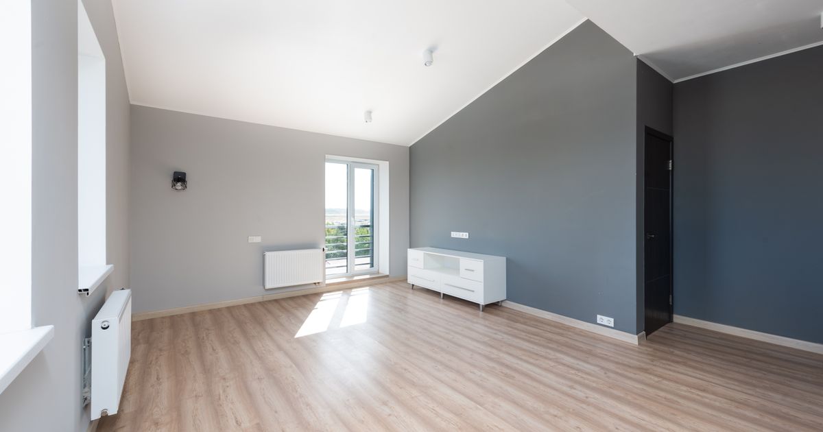 Wide-angle shot of a modern unfurnished apartment with wooden flooring and large windows.
