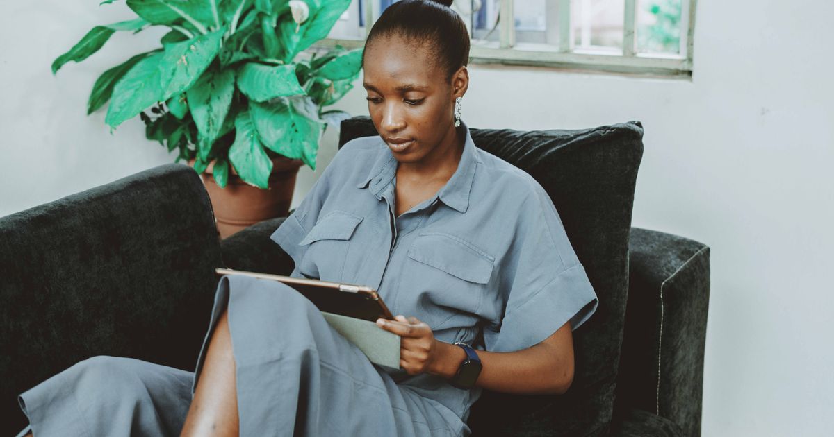 A woman sits on a sofa using a tablet, embodying modern remote work from a cozy living room setting.