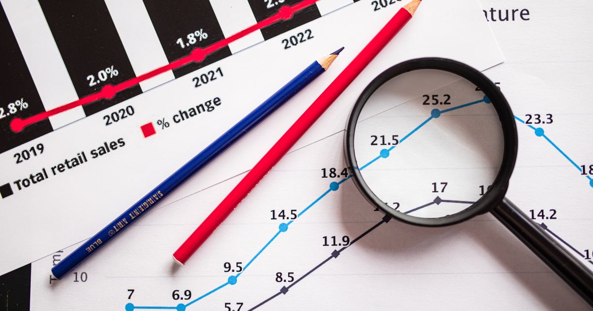 Magnifying glass and colored pencils on financial trend graphs highlighting sales growth.