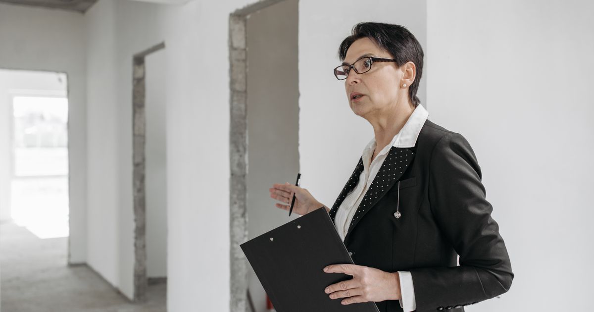 Woman in a suit holding a clipboard, inspecting an unfinished indoor construction site.
