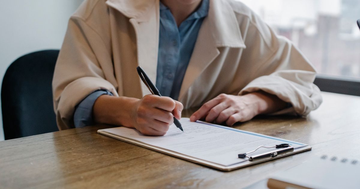 Crop young female unemployed job seeker filling questionnaire sitting at table during interview in office