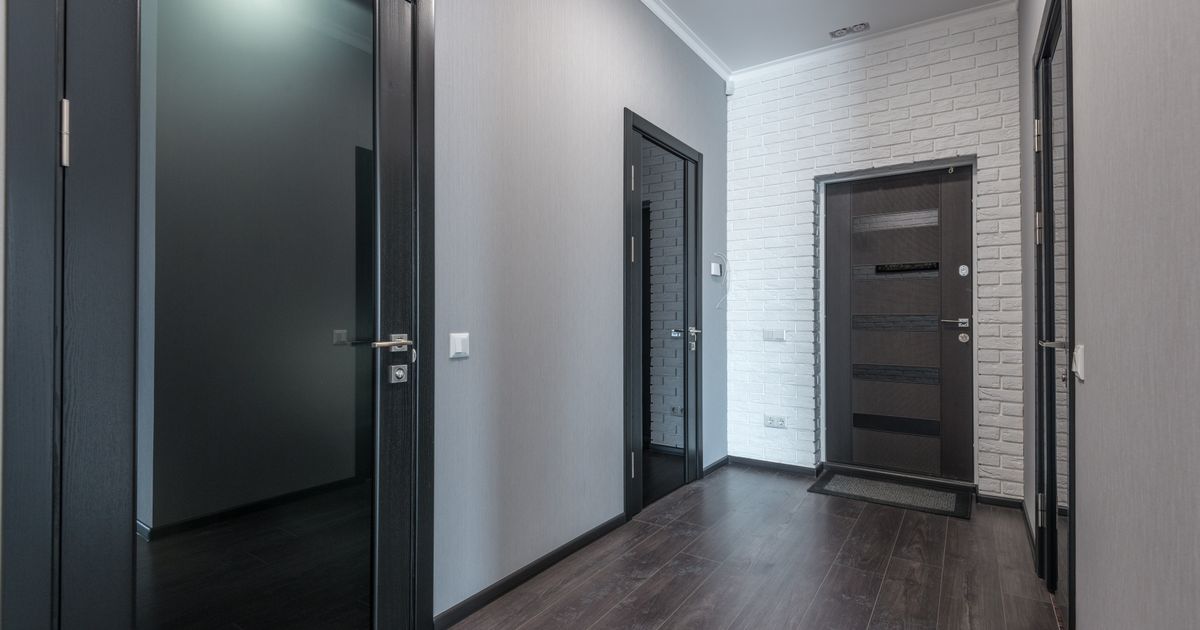 Interior of empty spacious corridor with laminate floor and black doors with glass parts and white ceiling and gray painted walls