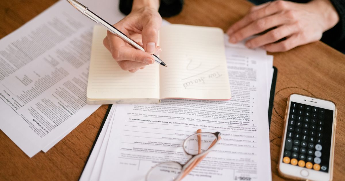 Close-up of a person writing in a notebook with documents and a calculator, managing finances.